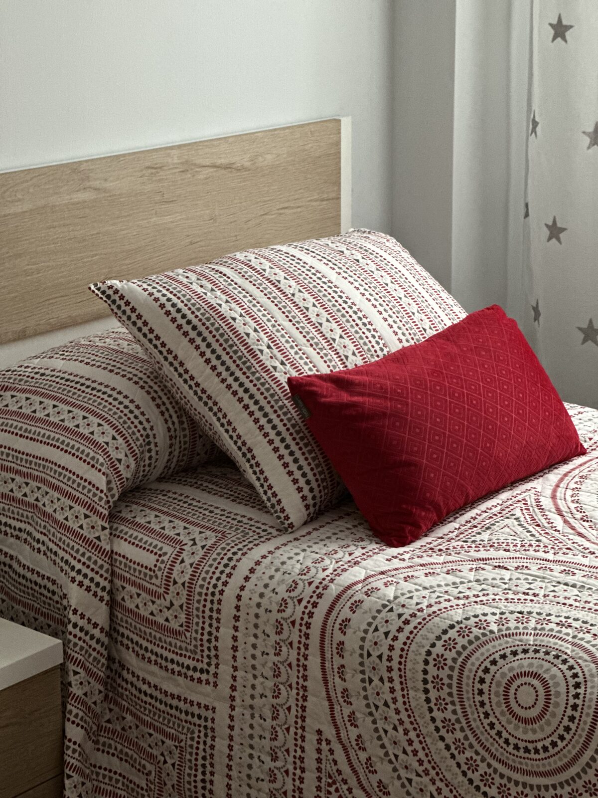 Detalle de cama individual con cabecero de madera y cojines