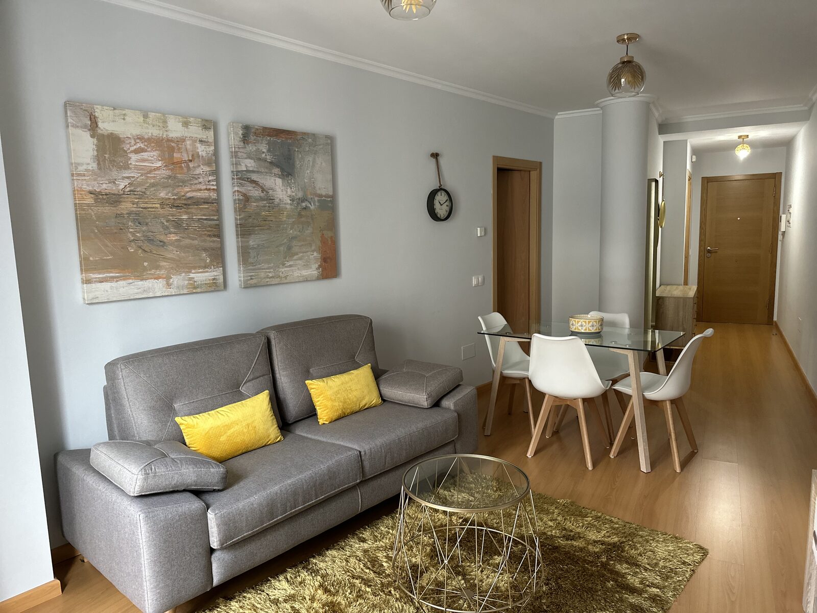Salón comedor con sofá gris, mesa de cristal y cuadros